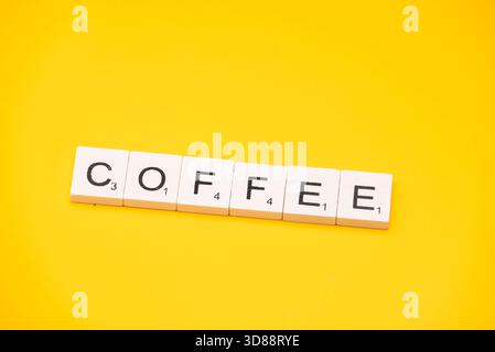 La parola CAFFÈ è stata scritta con tessere su sfondo giallo brillante. Foto Stock