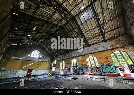 Ampio atrio interno con finestre ad arco e graffiti all'interno di un edificio industriale abbandonato. Foto Stock