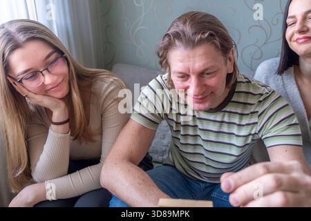 I membri della famiglia sono riuniti intorno a un tavolo, giocando a Jenga con blocchi di legno, condividendo sorrisi e risate, creando un caldo e.. Foto Stock