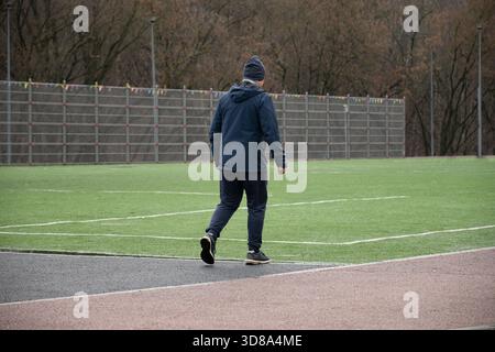 Uomo anziano attivo che cammina sul campo sportivo dopo l'allenamento all'aperto, mantenendo uno stile di vita sano e rimanendo fisicamente in forma. Palestra all'aperto Foto Stock