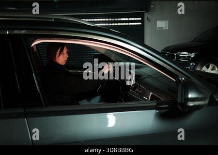 Una donna inizia a fare retromarcia all'interno di un garage con un display con telecamera posteriore che mostra le linee di parcheggio. Il momento mette in evidenza manovre sicure e moderne Foto Stock