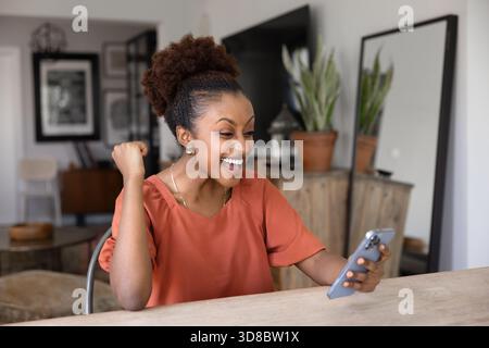 Allegra eccitata giovane donna africana che fissa lo smartphone Foto Stock