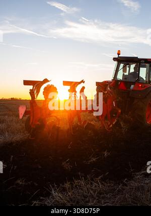 Trattore sul campo durante il tramonto. Il trattore ara il campo la sera al tramonto Foto Stock