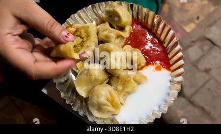 momos al vapore serviti con chutney rosso piccante e cagliata su un piatto usa e getta Foto Stock