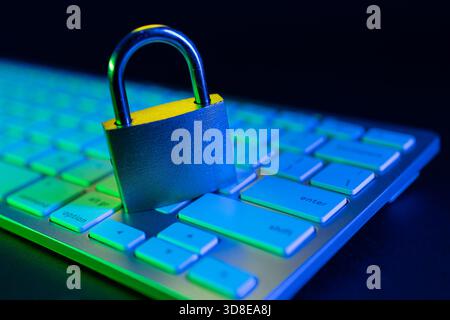 Un lucchetto poggia sulla tastiera di un computer illuminato da luci colorate. Questa scena evidenzia l'importanza della sicurezza Internet in un digitale moderno Foto Stock