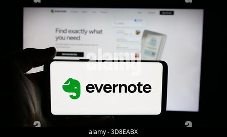 Stoccarda, Germania - 11-19-2025: Persona che detiene un cellulare con il logo della società di software per appunti Evernote sullo schermo davanti alla pagina web. Foto Stock
