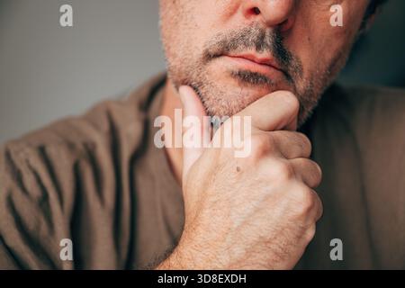 Primo piano di un uomo maturo e premuroso che tocca il mento, concetto di contemplazione e processo decisionale. Adulto adulto adulto adulto con abbigliamento casual con mano sul mento, Foto Stock