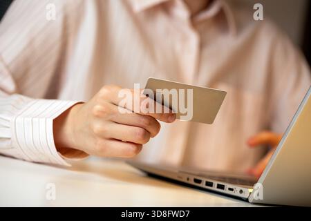 Primo piano di una persona che detiene una carta di credito mentre utilizza un laptop, che rappresenta acquisti online, pagamenti digitali e transazioni Internet sicure Foto Stock