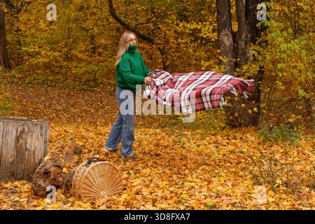 Donna che diffonde la coperta da picnic nell'Autumn Park. Preparatevi per un accogliente giorno d'autunno. Foto Stock