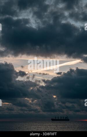 tranquilla scena marittima, tranquilla vista marittima con nave solitaria sotto il cielo ampio, tranquilla sagoma della nave che poggia sull'acqua ferma sotto Foto Stock