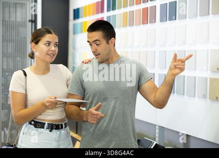 Coppia che parla e sceglie i colori della vernice sullo stand dei campioni in negozio Foto Stock