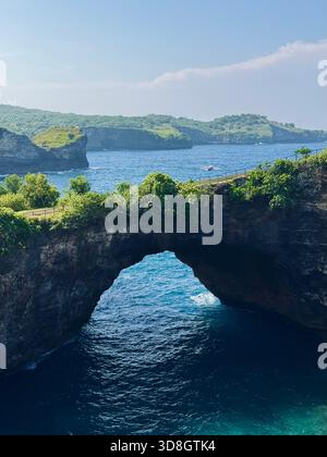 Posizione Sunset Rocks Pasih Uwug Beach Island Nusa Penida Bali Indonesia, arco di roccia balinaturale sul mare turchese, scogliere illuminate dal sole, vegetazione lussureggiante Foto Stock