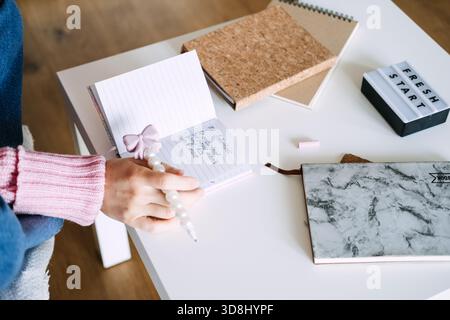 La persona siede alla scrivania scrivendo le intenzioni in un piccolo notebook accanto alla scatola luminosa che mostra UN NUOVO INIZIO. Risoluzioni per il nuovo anno, definizione degli obiettivi, pianificazione Foto Stock