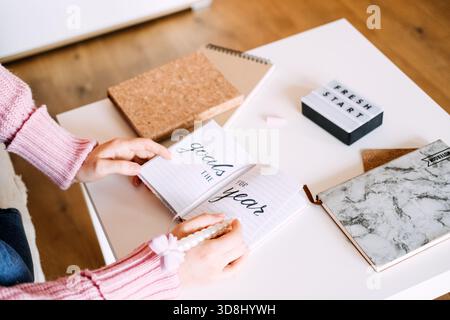 La persona siede alla scrivania scrivendo gli obiettivi per l'anno in un notebook accanto alla scatola luminosa che mostra UN NUOVO INIZIO. Risoluzioni per il nuovo anno, definizione degli obiettivi, pianificazione Foto Stock