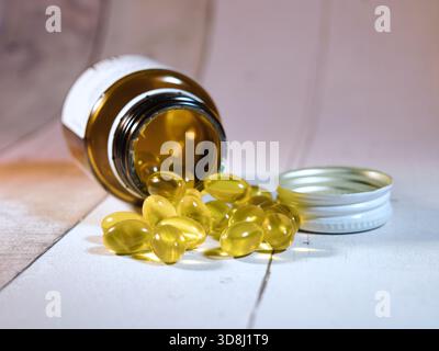 Pillole dorate che fuoriescono dalla bottiglia Medicina - primo piano di capsule softgel dorate che fuoriescono da una bottiglia di vetro ambrato su una superficie di legno chiaro. Idea Foto Stock