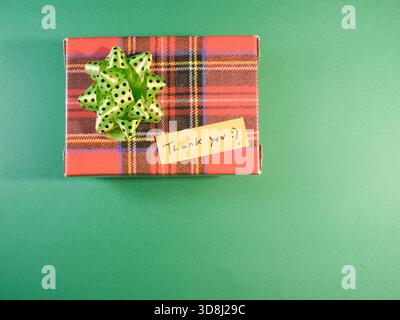 Regalo a quadri con nota di ringraziamento - Vista dall'alto di una scatola regalo a quadri legata a un arco a pois verde e una nota di ringraziamento su un retrogro verde vivace Foto Stock
