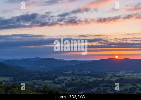 Il sole si immerge dietro le lontane catene montuose, dipingendo il cielo serale con colori caldi Foto Stock