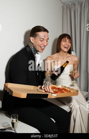 Una giovane coppia si gode una serata romantica con pizza e champagne, piena di risate e gioia. Foto Stock