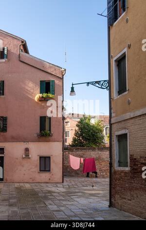 Appartamenti rosa e piccolo cortile con lavanderia appesa su una linea di stoffa in una tranquilla zona residenziale di Venezia, Italia. Foto Stock
