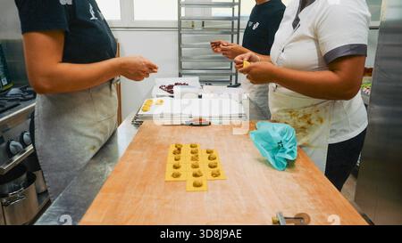 Le mani dello chef impastano e modellano la pasta gialla su una superficie rustica in legno, mostrando il meticoloso processo di preparazione del cibo fatto a mano in una b Foto Stock
