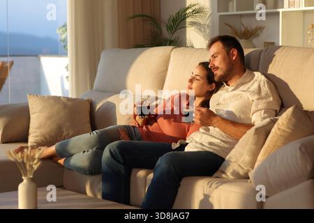 Una coppia innamorata che beve un caffè guardando lontano seduto su un divano di casa Foto Stock