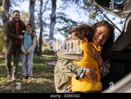 Una famiglia gioiosa trascorre del tempo in un parco, abbracciando e ridendo mentre si gode il caldo sole. Gli alberi circondano la scena giocosa. Foto Stock