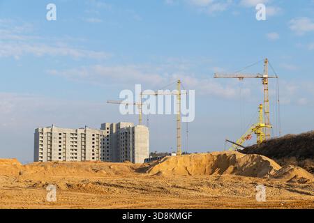 Diverse gru a torre si stagliano su un grande nuovo e alto sviluppo residenziale, con edifici in cemento non finiti e un cantiere in terra battuta Foto Stock