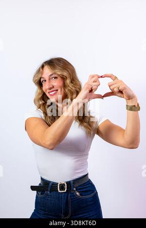 Giovane donna sorridente, mostra un gesto cardiaco con le mani, esprime amore e cura Foto Stock