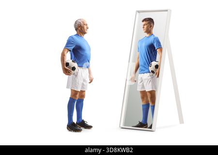 Uomo anziano con un pallone da calcio e guardando il sé più giovane in uno specchio isolato su sfondo bianco Foto Stock