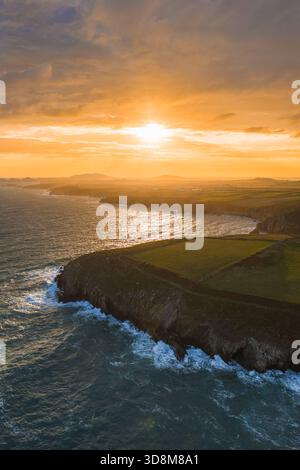 Vista aerea della luce del sole dorata che bacierà la costa frastagliata dove la terra verde incontra il mare selvaggio, St. Davids, Galles, Regno Unito. Foto Stock