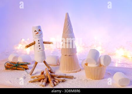 Stravagante scena al coperto con un pupazzo di neve marshmallow su arti di pretzel accanto a un albero di Natale a cono di waffle, circondato da bastoncini di cannella e polvere Foto Stock