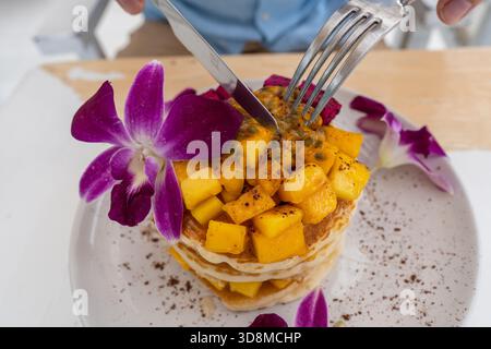 Gustosi pancake con frutta tropicale in un piatto su un tavolo in un caffè, primo piano. Colazione sana. Deliziosi pancake con mango, frutta di drago e pass Foto Stock
