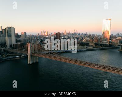Vista aerea del maestoso Ponte di Brooklyn attraversa l'East River, collegandosi allo skyline della città sotto il soffice bagliore del tramonto, New York, N Foto Stock