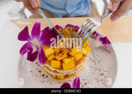 Gustosi pancake con frutta tropicale in un piatto su un tavolo in un caffè, primo piano. Colazione sana. Deliziosi pancake con mango, frutta di drago e pass Foto Stock