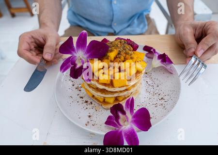 Gustosi pancake con frutta tropicale in un piatto su un tavolo in un caffè, primo piano. Colazione sana. Deliziosi pancake con mango, frutta di drago e pass Foto Stock
