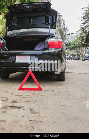 Auto nera con bagagliaio aperto che mostra un triangolo segnaletico rosso sul marciapiede Foto Stock