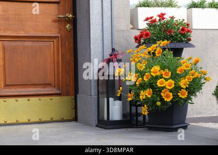 Giallo brillante Gaillardia e fiori di Rudbeckia arancio-rosso disposti in vasi decorativi da un ingresso di casa in legno. Piante colorate che creano un Foto Stock