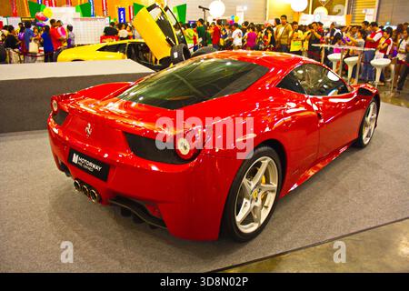 Vista posteriore della lucente Ferrari 458 Italia rossa in mostra all'affollato salone dell'automobile al coperto, circondato da folle eccitate e altre supercar. Foto Stock