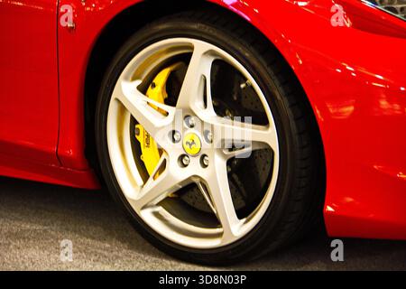 Primo piano di una ruota Ferrari supercar con cerchioni in metallo lucido, pinze dei freni gialle vibranti e pneumatici Pirelli neri contro la carrozzeria rossa,... Foto Stock