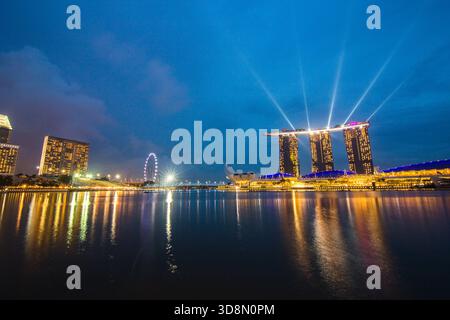 Futuristico skyline della metropoli con torri luccicanti e ruota panoramica, che si specchia sulle acque calme, creando un'atmosfera serena serale. Foto Stock