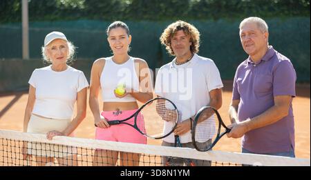 Un gruppo di amici sta vicino alla rete su un campo da tennis Foto Stock