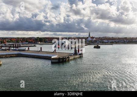 Terminal dei traghetti, porto con paesaggio urbano, chiesa di San Nicola, cielo nuvoloso, raggi del sole, Ronne, Bornholm, Mar Baltico, Danimarca Foto Stock