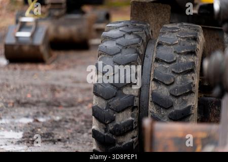 Ruote per macchinari per impieghi gravosi posizionate su un cantiere all'aperto fangoso, che rivelano un battistrada in gomma profondo, l'usura superficiale e gli elementi utilizzati per le apparecchiature industriali Foto Stock