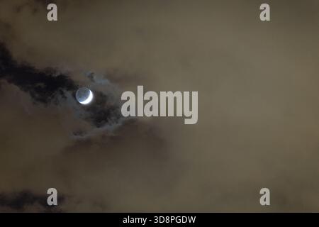 L'illuminazione di Earthshine crea un brillante frammento di luce sulla superficie della luna, formando una luna crescente mistica che galleggia attraverso le nuvole serali. Foto Stock