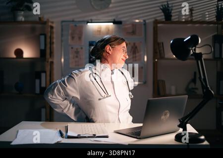Giovane infermiera o medico che soffre di mal di schiena dopo un lungo lavoro al computer, soffre sul posto di lavoro. assistenza sanitaria e medica Foto Stock