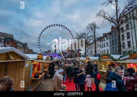 Bruxelles, Belgio - 30 novembre 2025: Folle che camminano attraverso il mercatino di Natale delle meraviglie invernali, con la ruota panoramica illuminata che si innalza sopra le festività Foto Stock