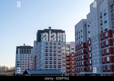 Moderni ed alti edifici di appartamenti con facciate grigie, bianche e rosse si innalzano sotto un cielo azzurro, una nuova area residenziale urbana Foto Stock