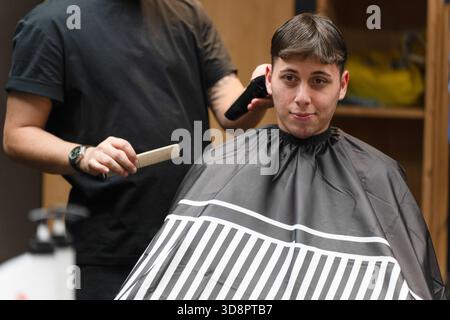 Barbiere tagliando i capelli a un cliente con pettine e regolacapelli Foto Stock
