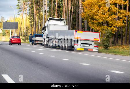 Vista del semirimorchio bianco con rimorchio a pianale vuoto fermo sulla spalla autostradale. Auto rossa parcheggiata, persona in piedi vicino al veicolo. Autunno per Foto Stock