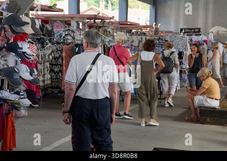 Dubrovnik. Croazia - 2 dicembre 2025: Un gruppo di turisti visto da dietro mentre curiosano tra le bancarelle di abbigliamento e souvenir, tra cui i cappelli croati, presso un Foto Stock